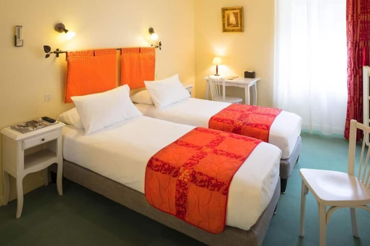 A hotel room with two beds, a desk, a chair, and a small table.