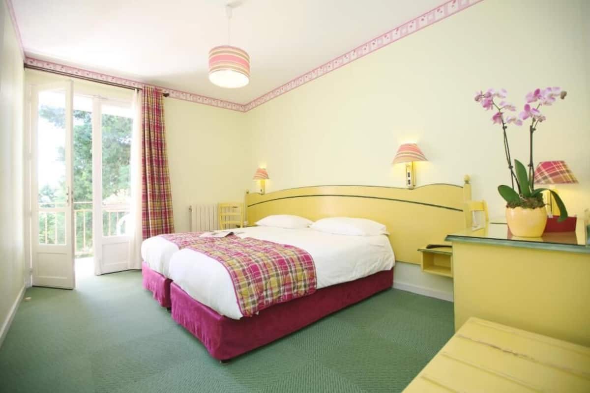 Une chambre à coucher avec un lit, deux lampes de chevet, une table de nuit, une orchidée en pot et une vue à travers une porte vitrée.