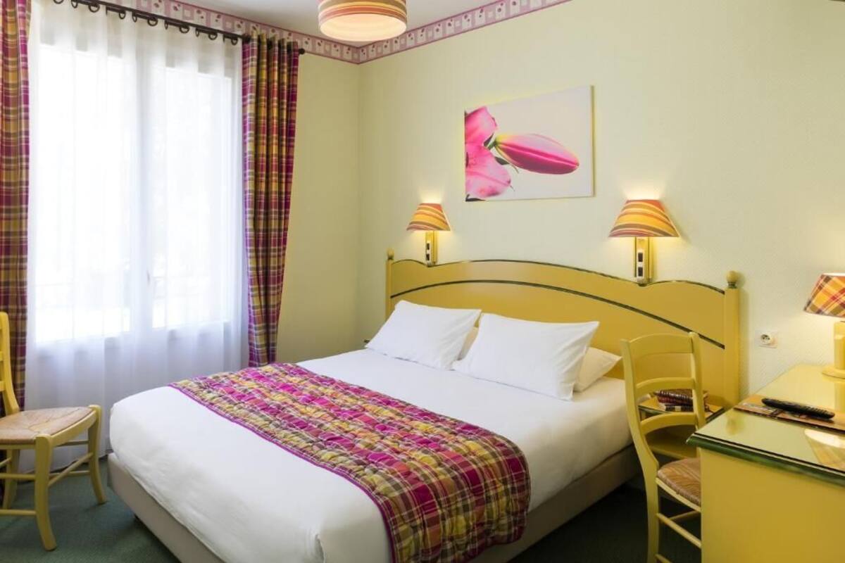 A hotel room with a bed, two bedside lamps, a desk, a chair, and a window with curtains.