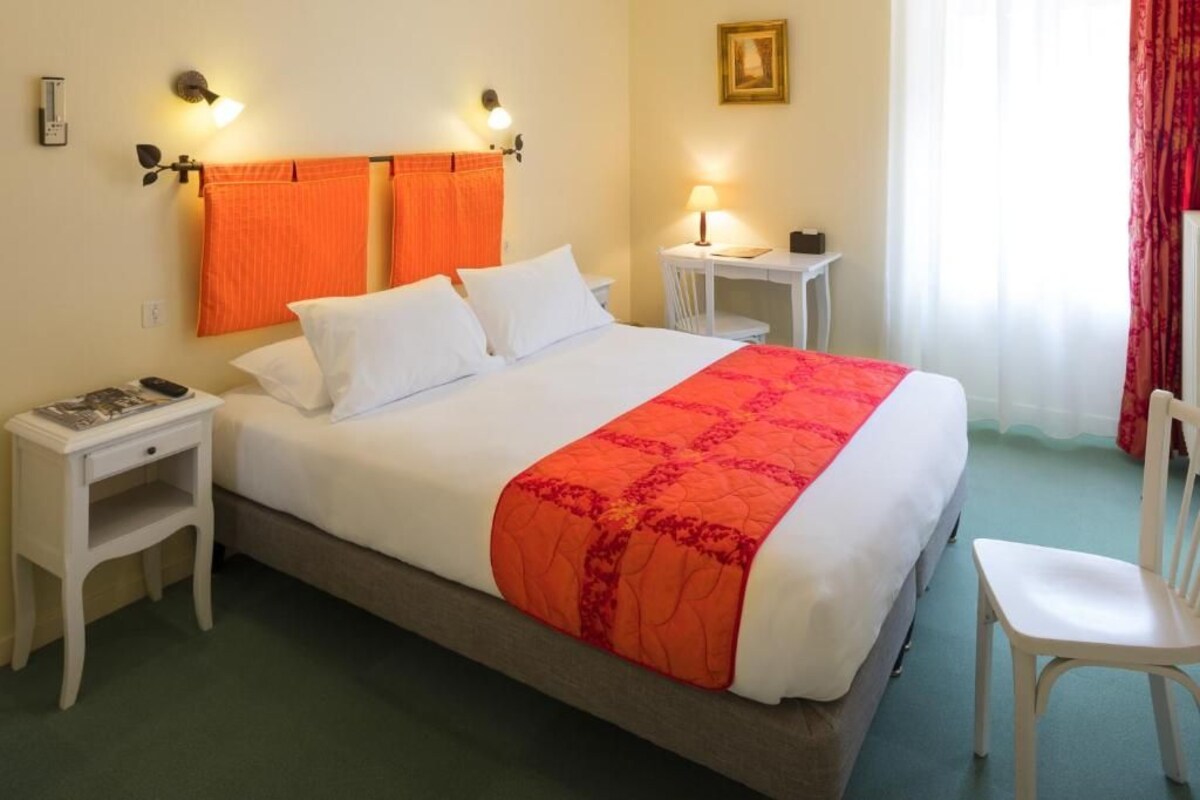 A hotel room with a bed, bedside tables, a chair, a desk, and a lamp.