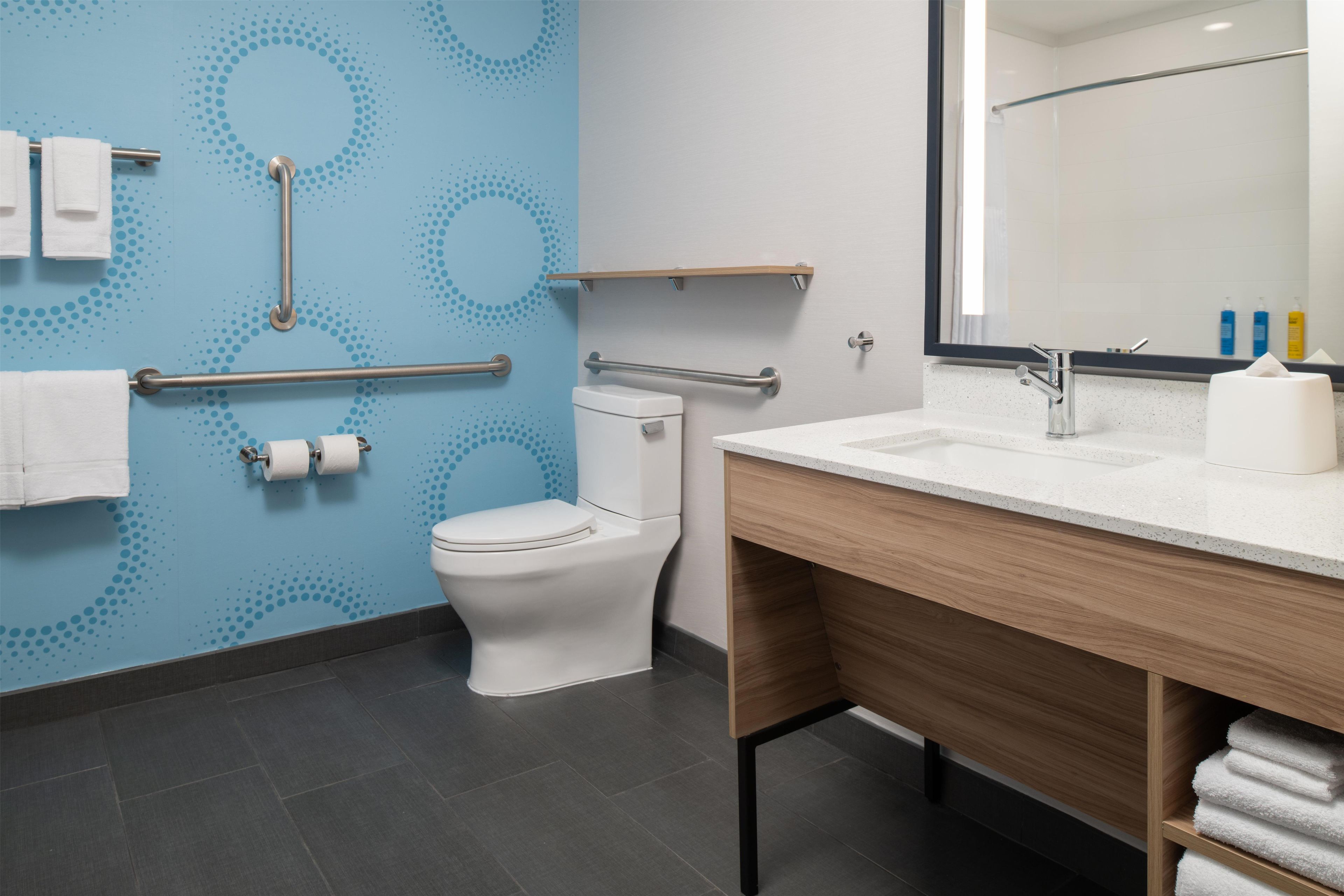 A modern bathroom with a blue wall, a white toilet, a wooden vanity, and a mirror.