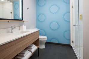 A bathroom with a wooden vanity, a white toilet, and a blue patterned wall. - Tru by Hilton El Paso Airport (El Paso)