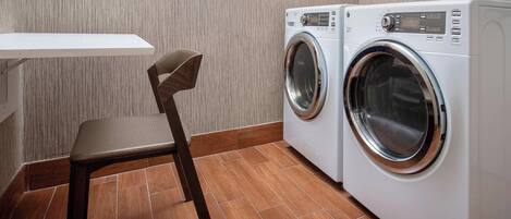 A laundry area with a washing machine and dryer, a chair, and a wooden floor.