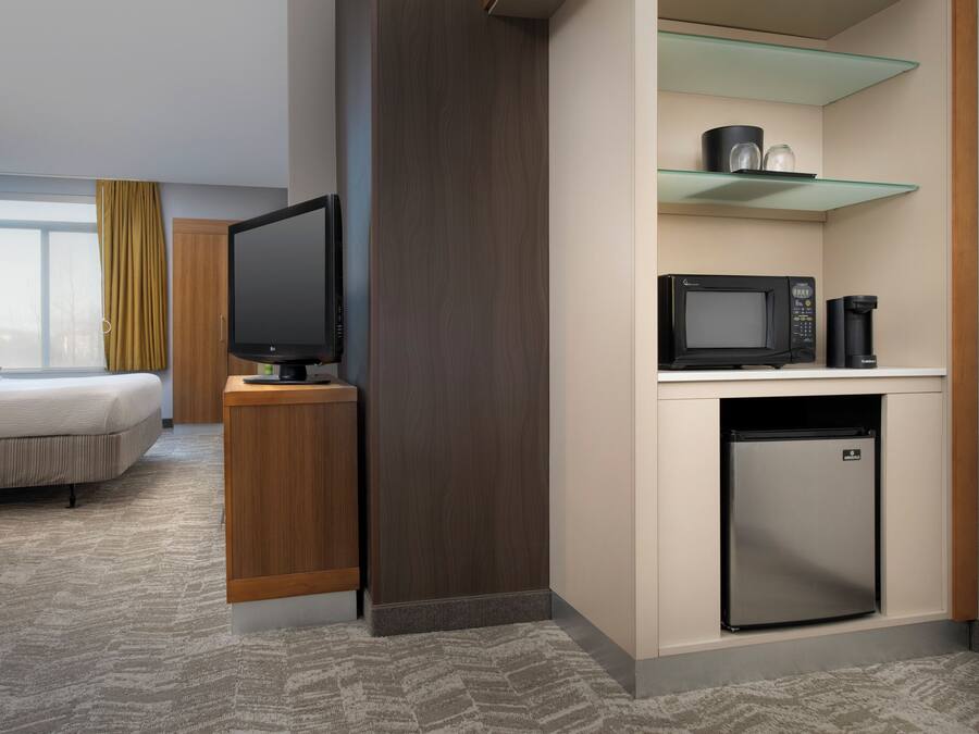 A hotel room with a bed, a television, a microwave, a coffee maker, and a mini-fridge.