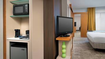 Habitación de hotel con cama, televisor, microondas, cafetera y refrigerador pequeño.