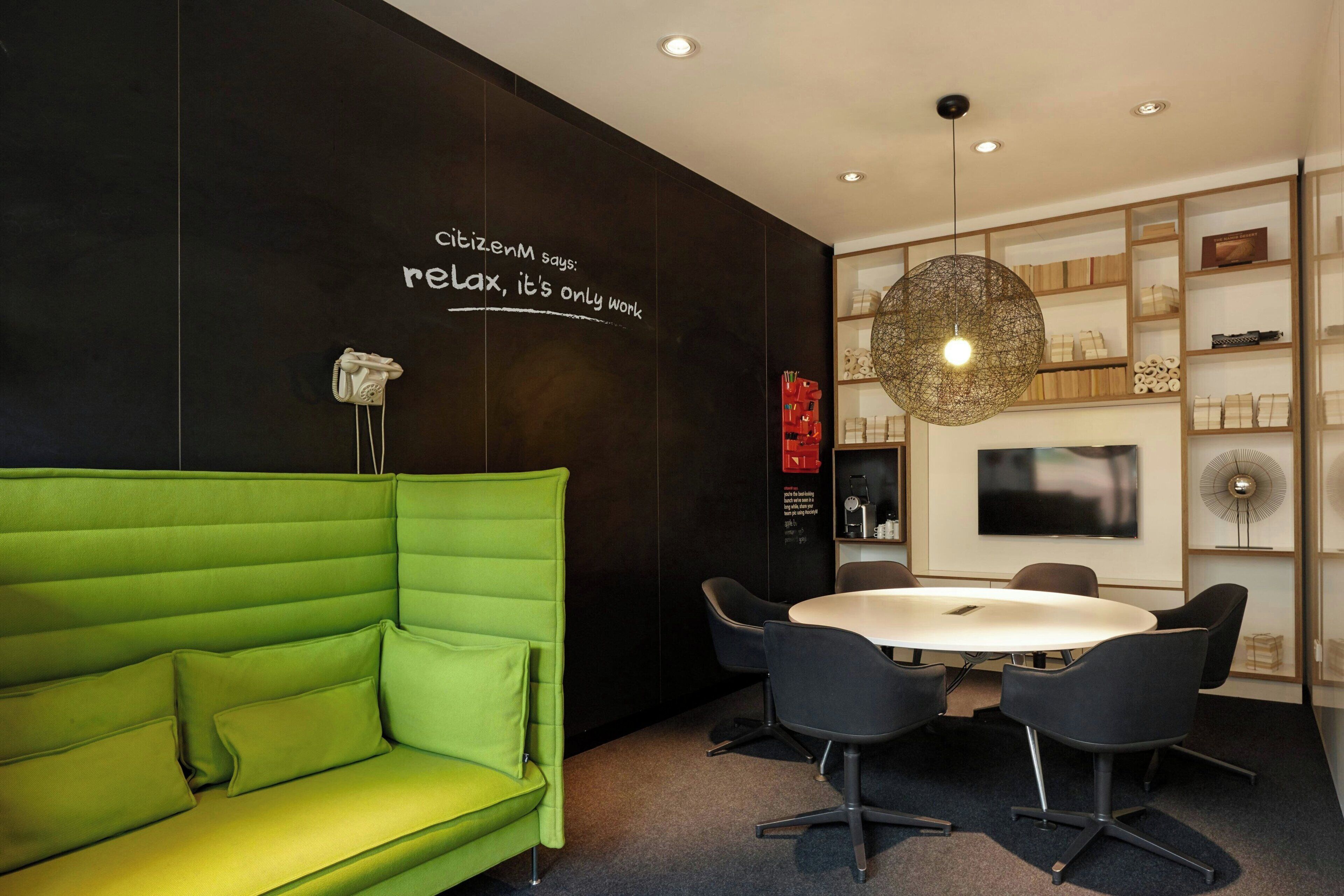 A modern meeting room with a green sofa, a round table, and chairs.