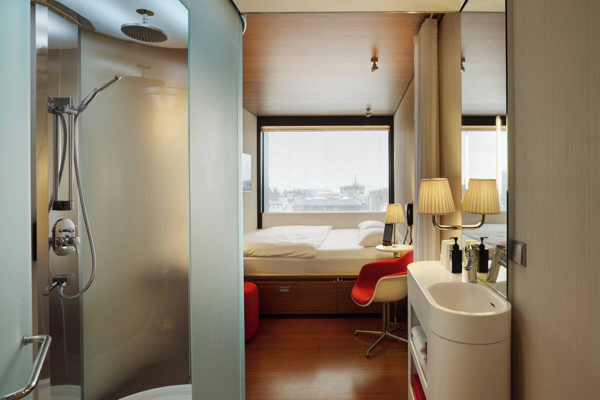 A modern hotel room with a shower, a bed, a desk, and a window with a city view.