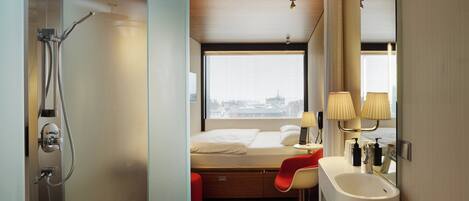Une chambre d’hôtel moderne équipée d’une douche, d’un lit, d’un bureau et d’une fenêtre donnant sur la ville.