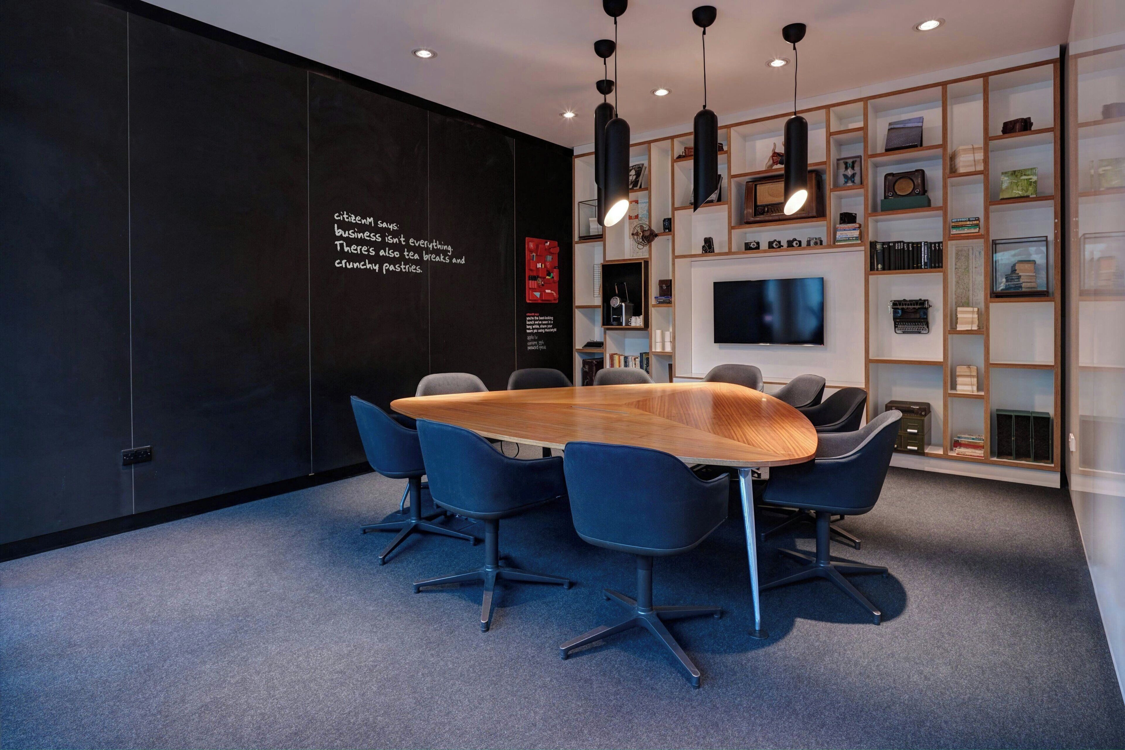 A modern conference room with a large oval table, blue chairs, and a black wall with text.
