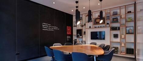 A modern conference room with a large oval table, blue chairs, and a black wall with text.