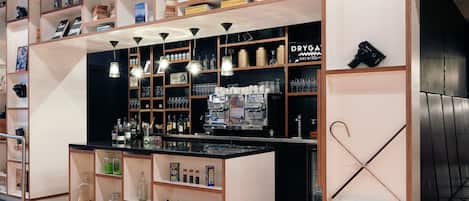 A bar area with shelves stocked with various bottles and glasses, espresso machines, and a display of books and magazines.