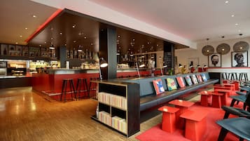 A modern bar area with a long counter, stools, and a seating area with red tables and benches.