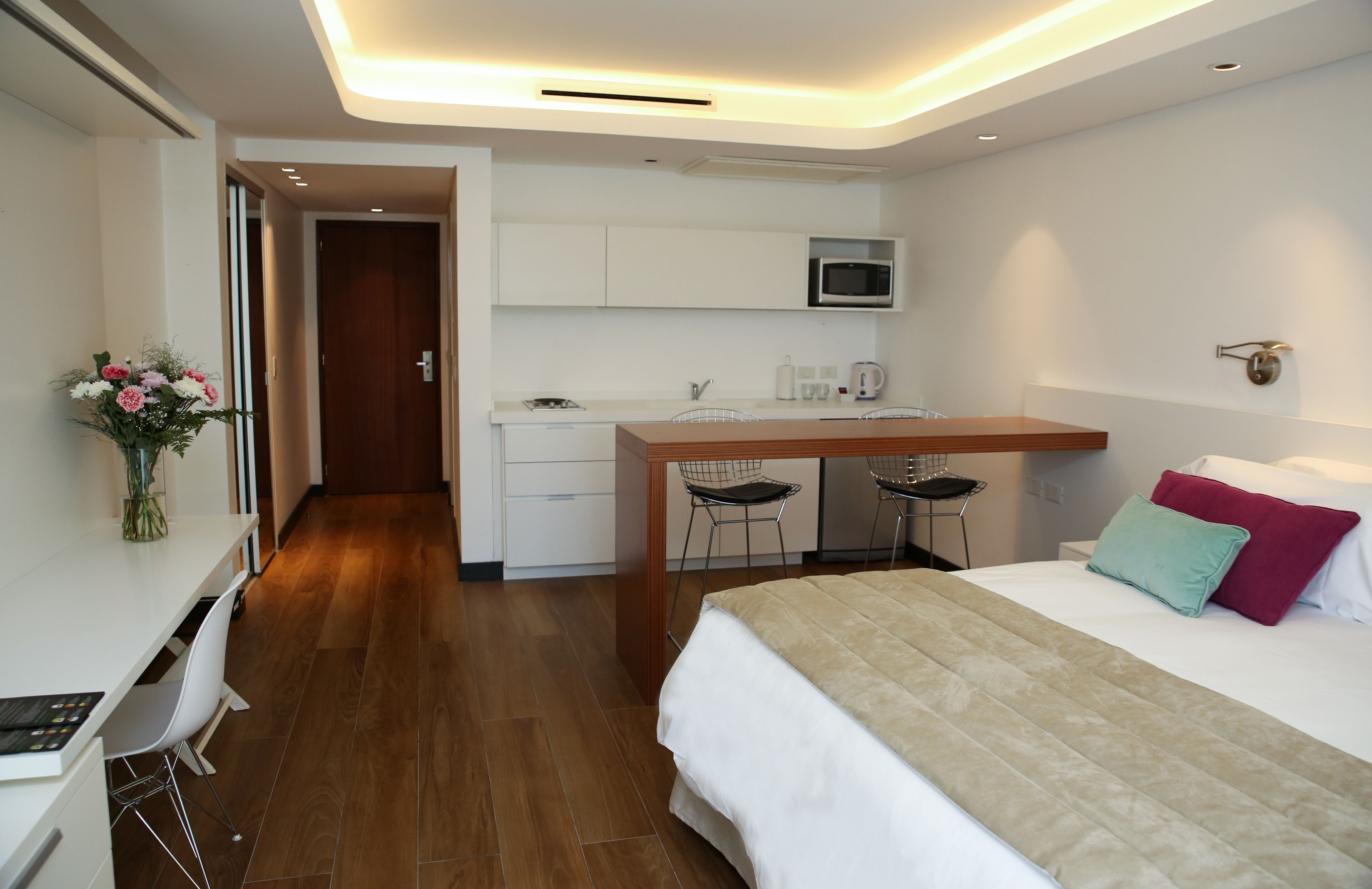 Una habitación de hotel moderna con una cama, un escritorio con dos sillas, un microondas y una pequeña cocina.