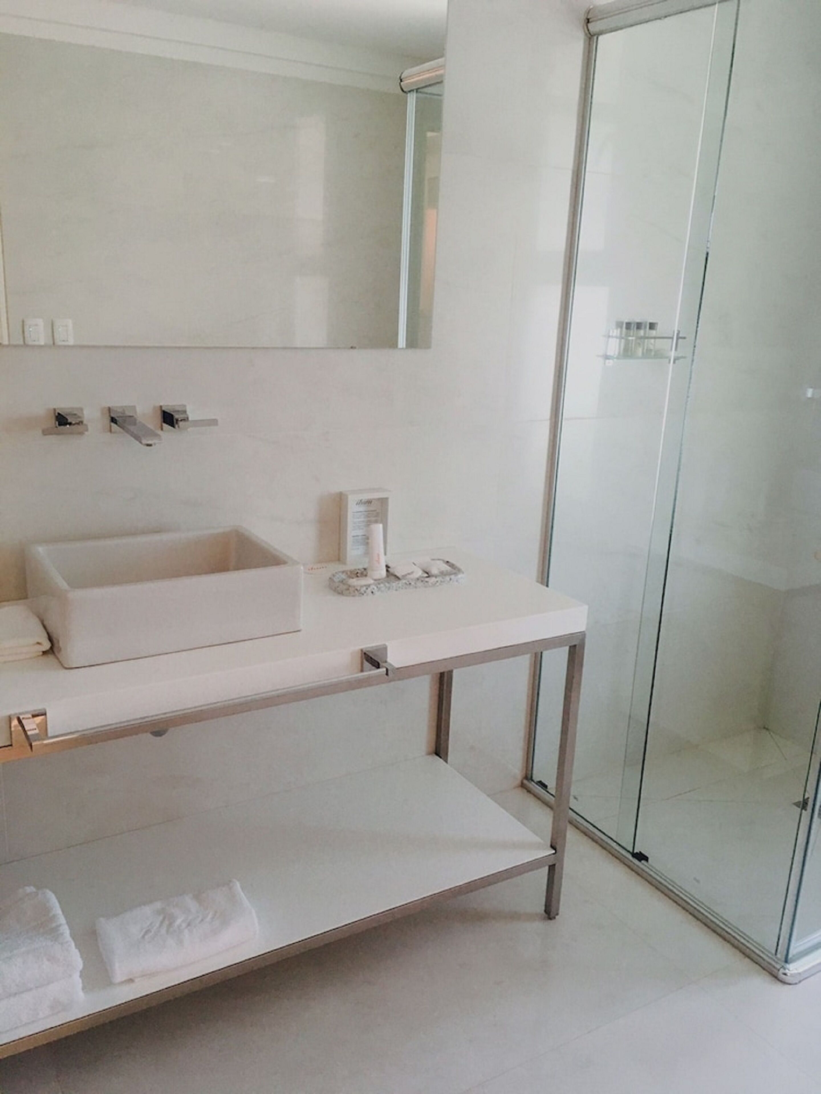 A modern bathroom with a white sink, mirror, and glass shower enclosure.
