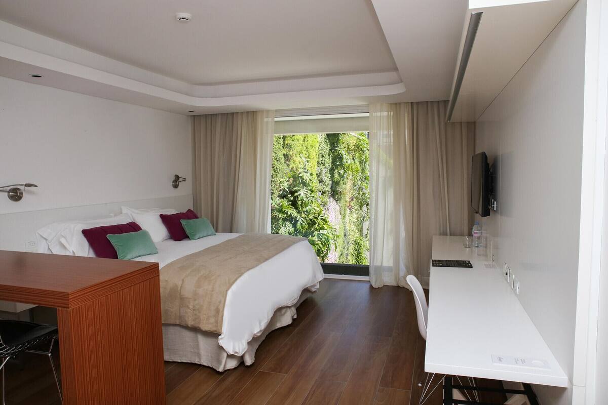 Habitación de hotel con cama, escritorio, televisor y vistas a zonas verdes.