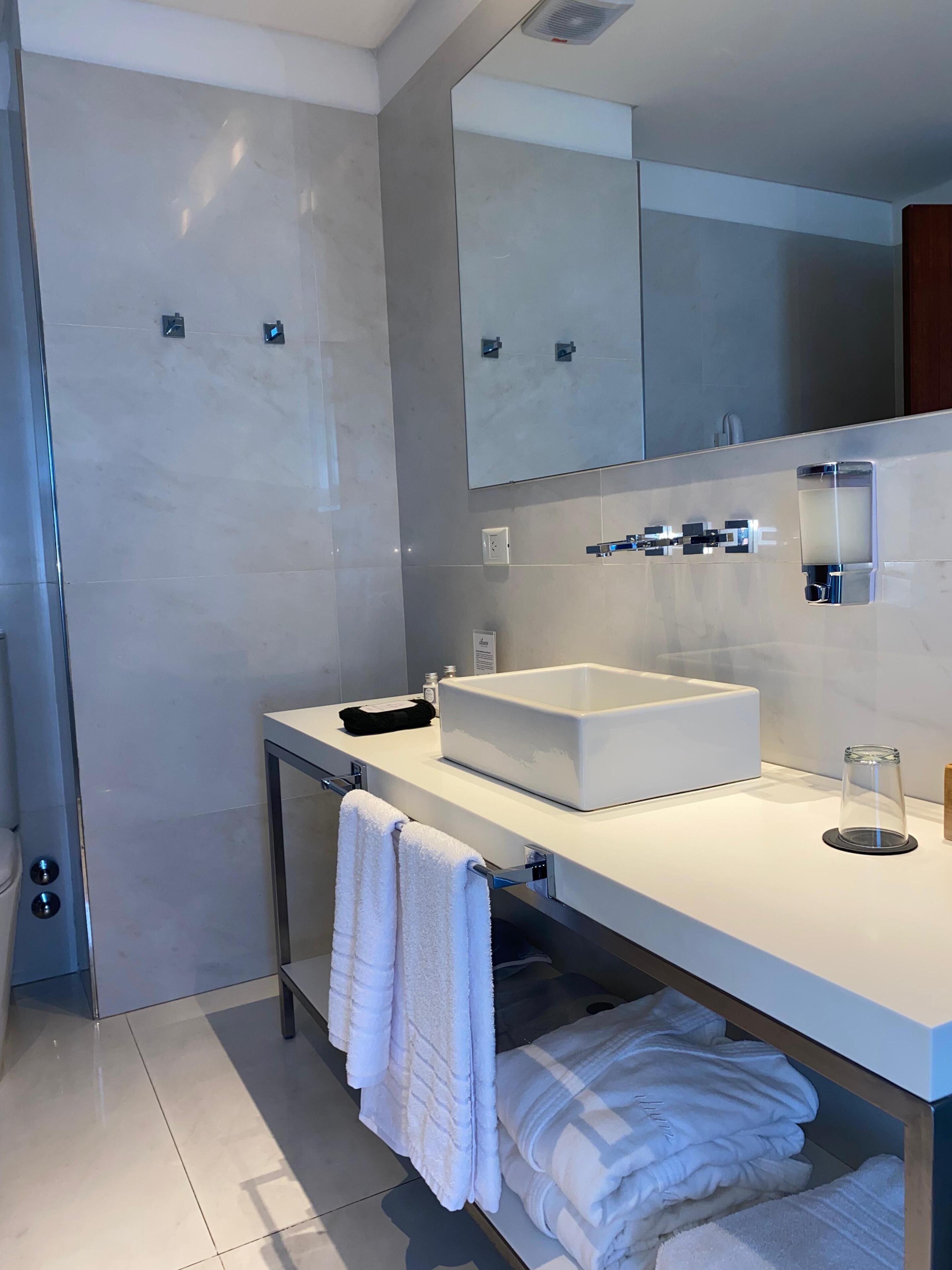 Un baño moderno con un espejo grande, lavamanos blanco y toallero.