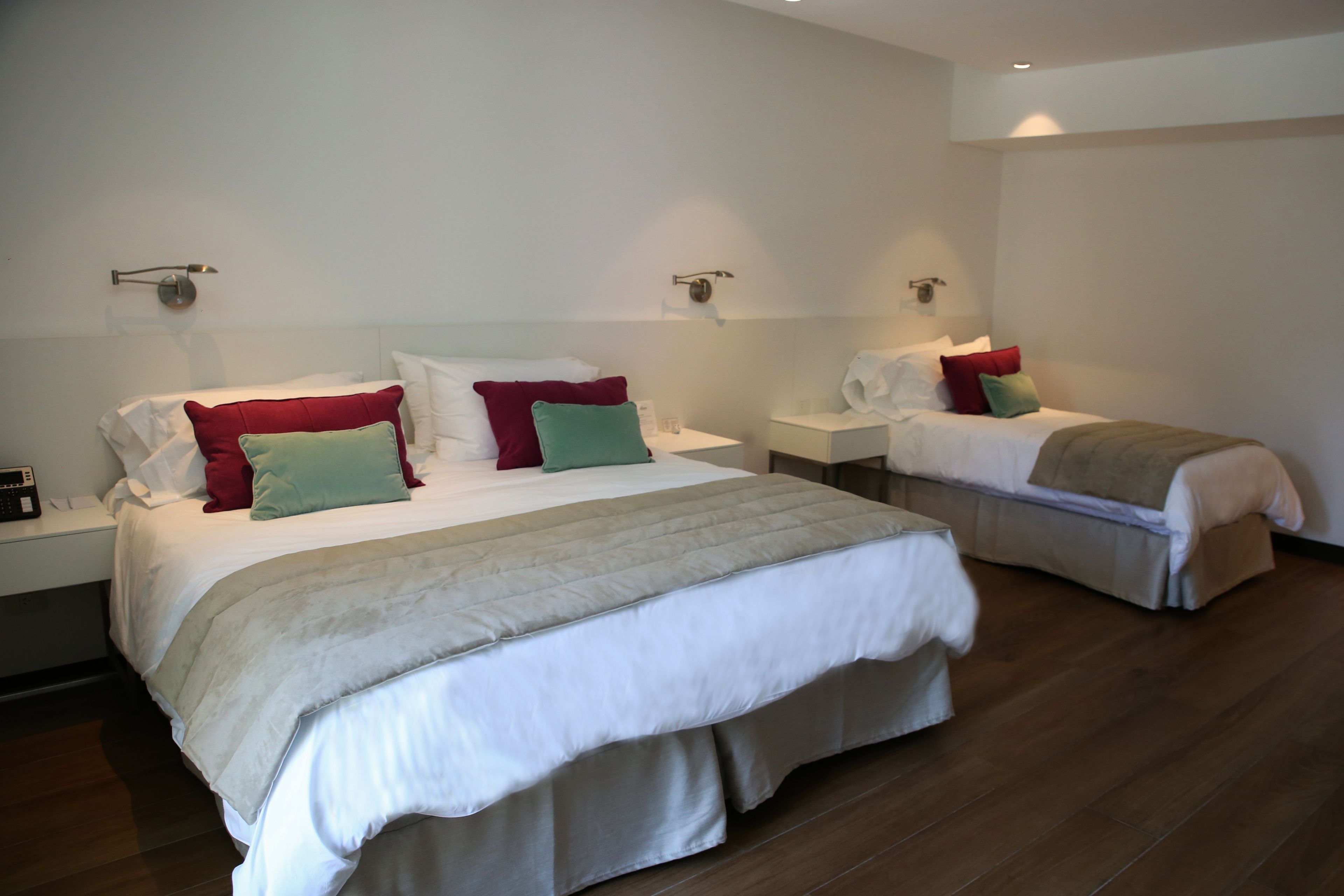 A hotel room with two beds, a nightstand, and a wall-mounted lamp.