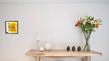 A wooden table with a glass, a white vase with flowers, a Buddha statue, and a framed picture on the wall.