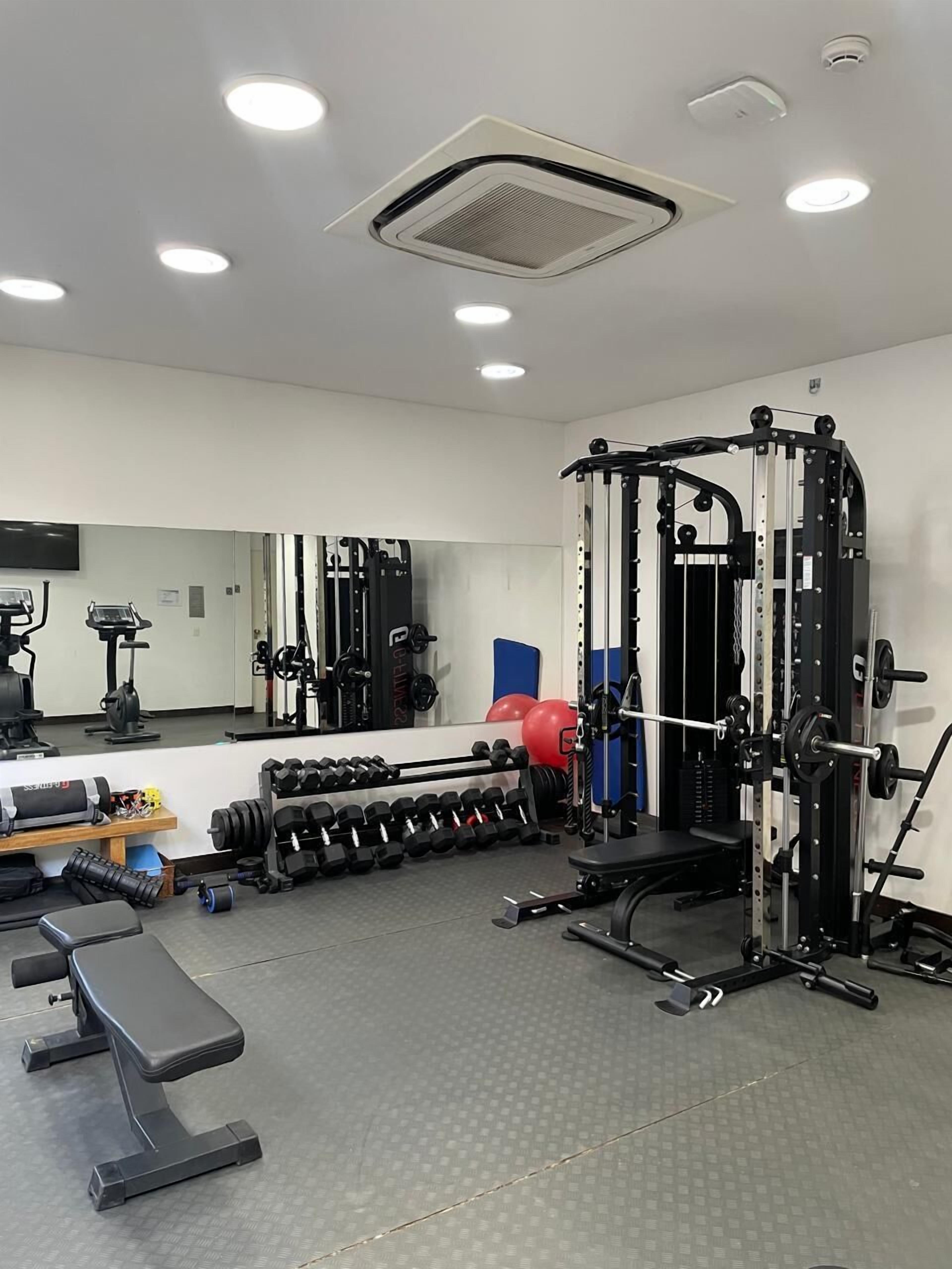 A gym with a bench press, dumbbells, a squat rack, and a mirror.