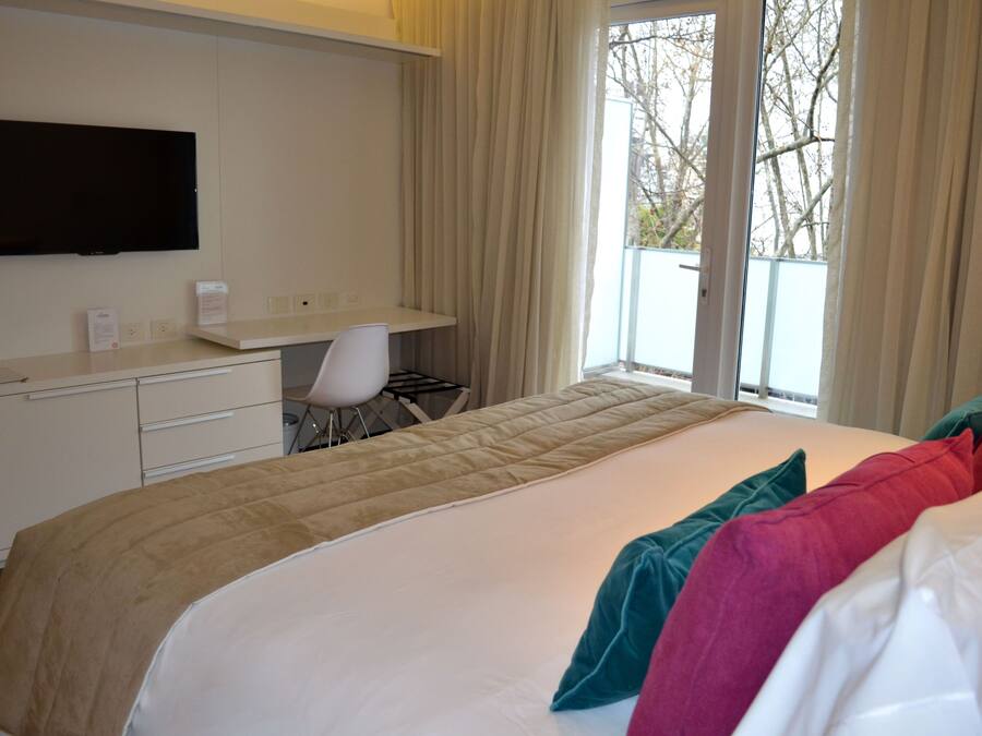 Habitación de hotel con cama, escritorio, silla, televisor y ventana con cortinas.