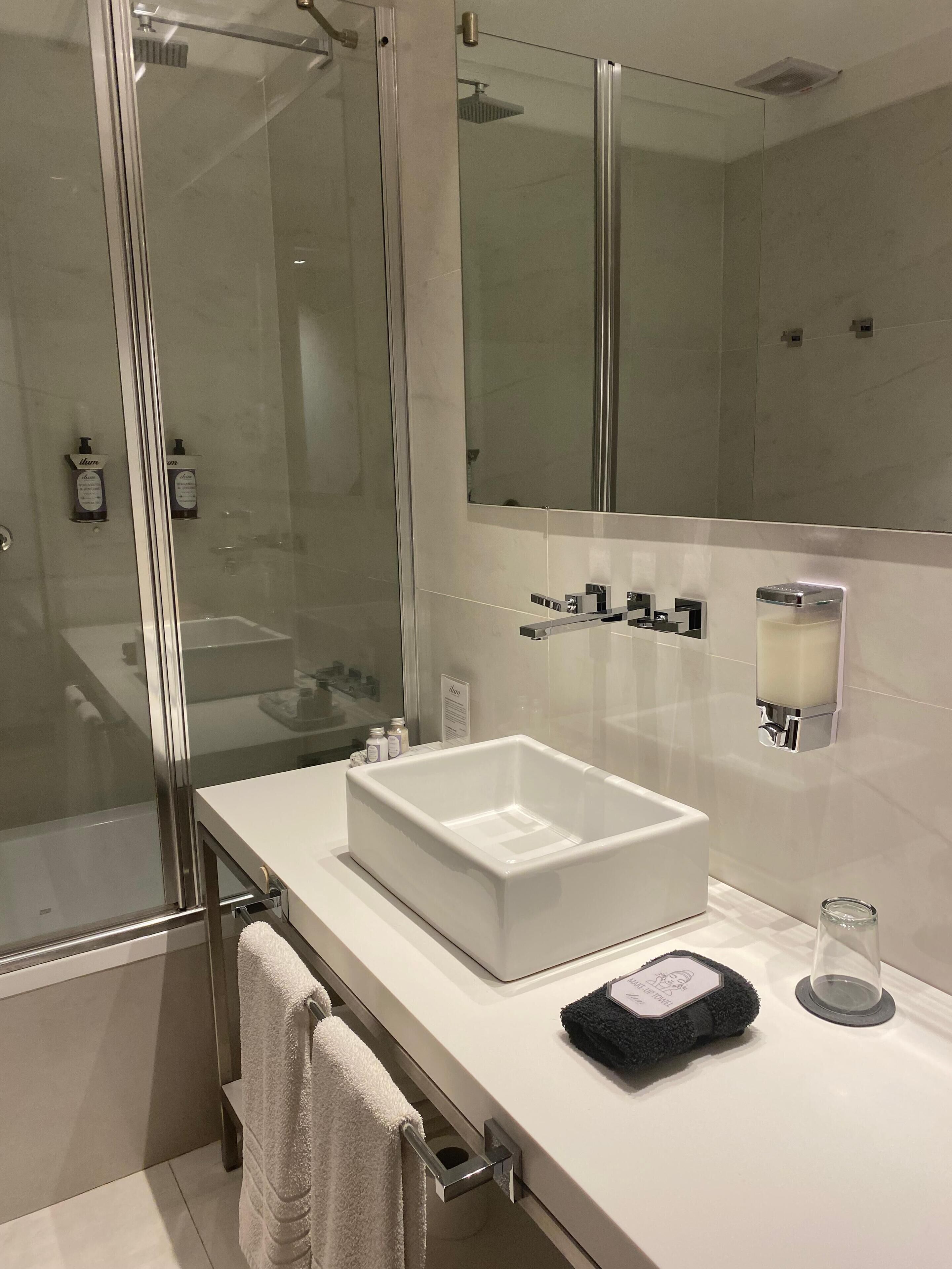 Un baño moderno con ducha de vidrio, lavamanos blanco y espejo grande.
