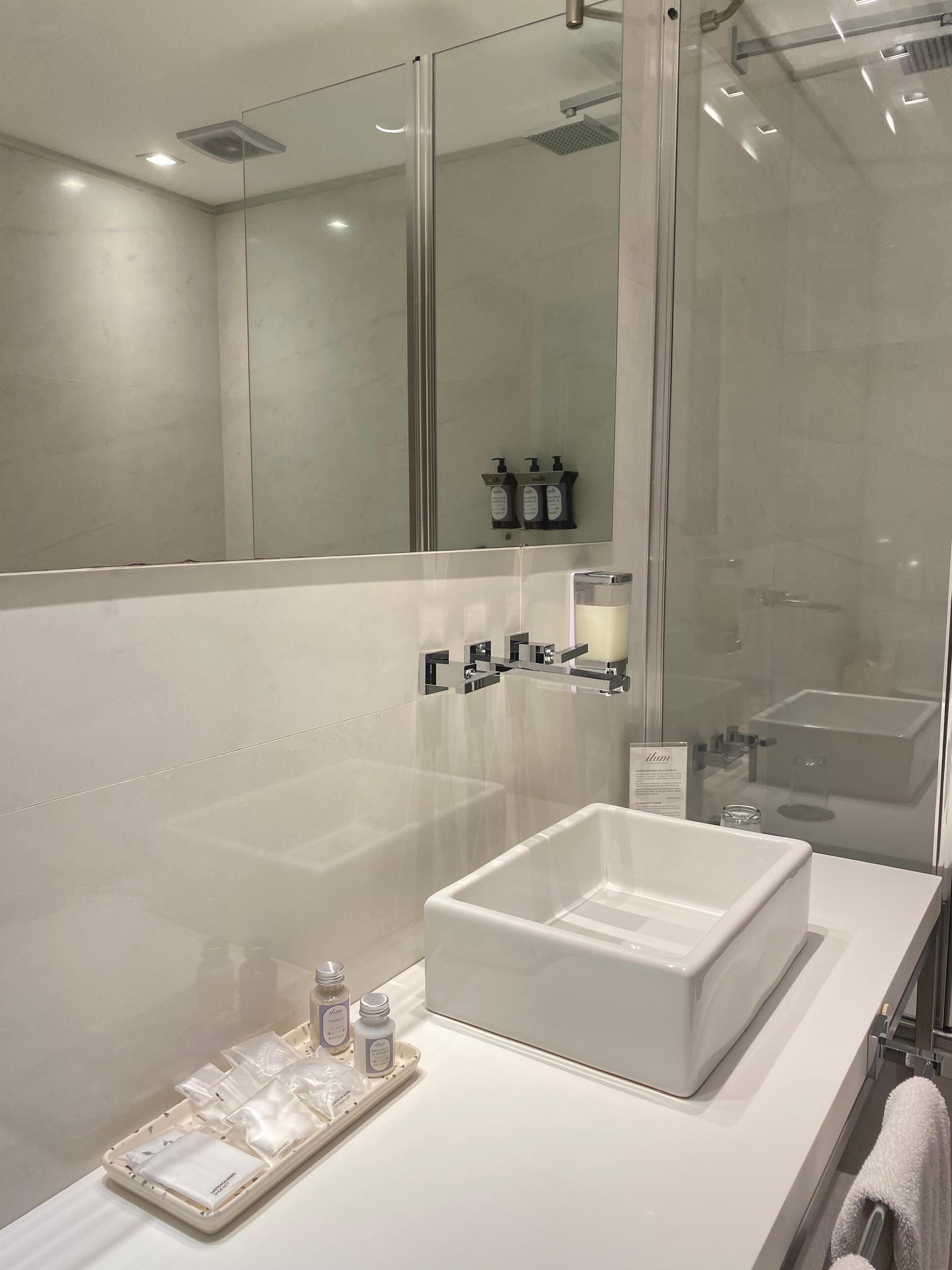 Ein modernes Badezimmer mit großem Spiegel, weißem Waschbecken und einer Duschkabine aus Glas.