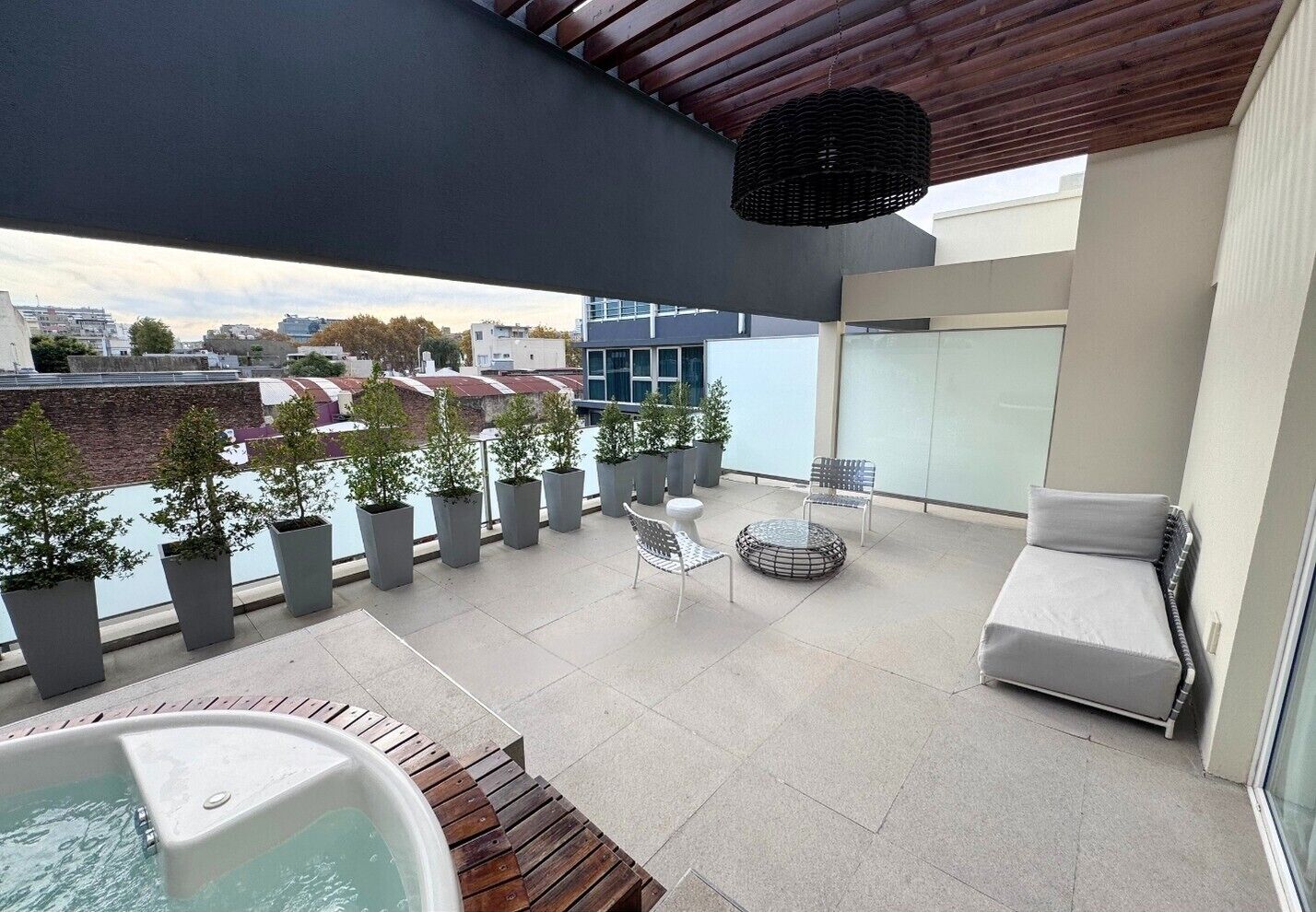 Una terraza en la azotea con un jacuzzi, zona de estar, plantas en macetas y vistas de la ciudad.