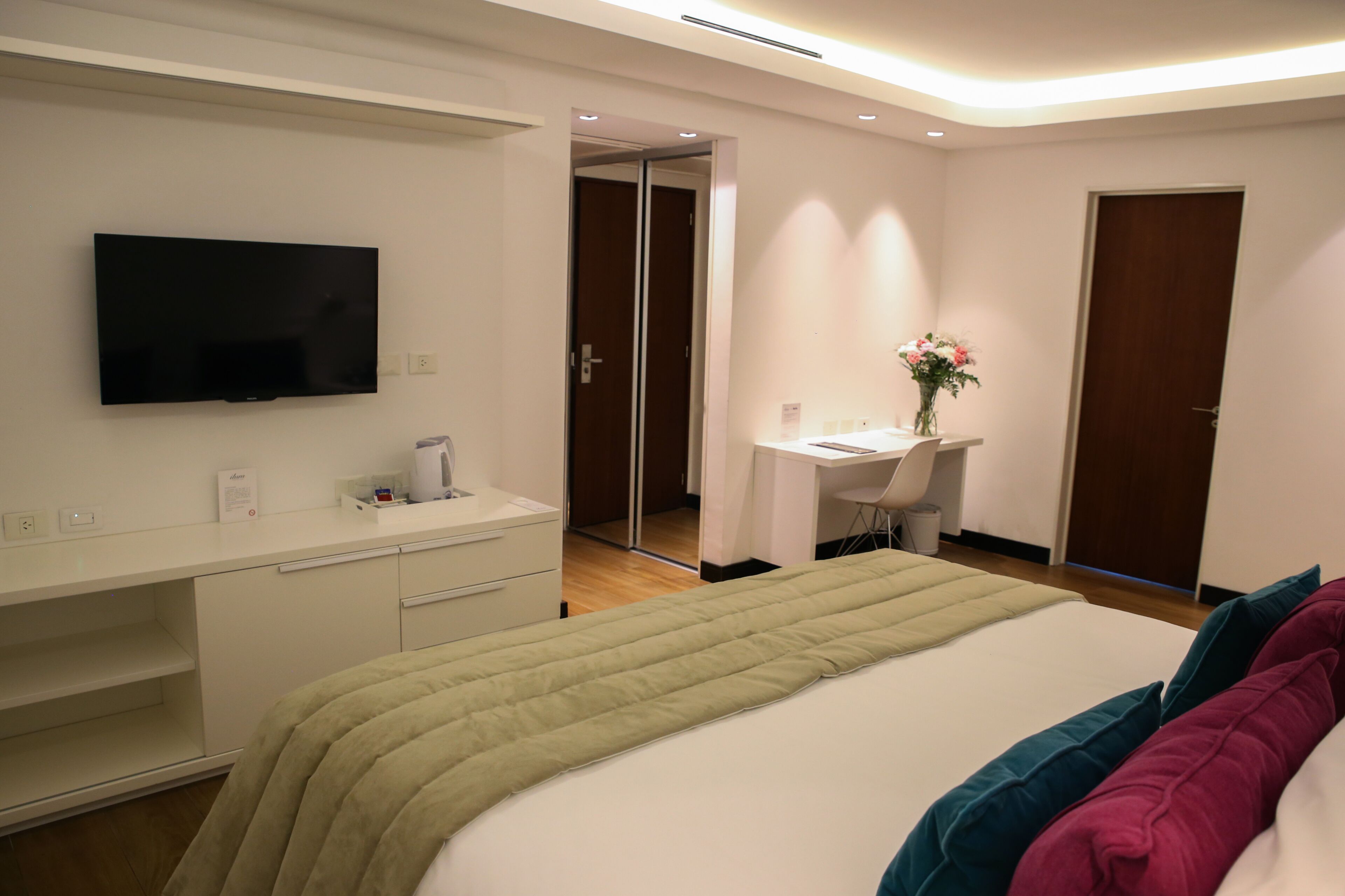A hotel room with a bed, a desk, a chair, a television, and a mirror.