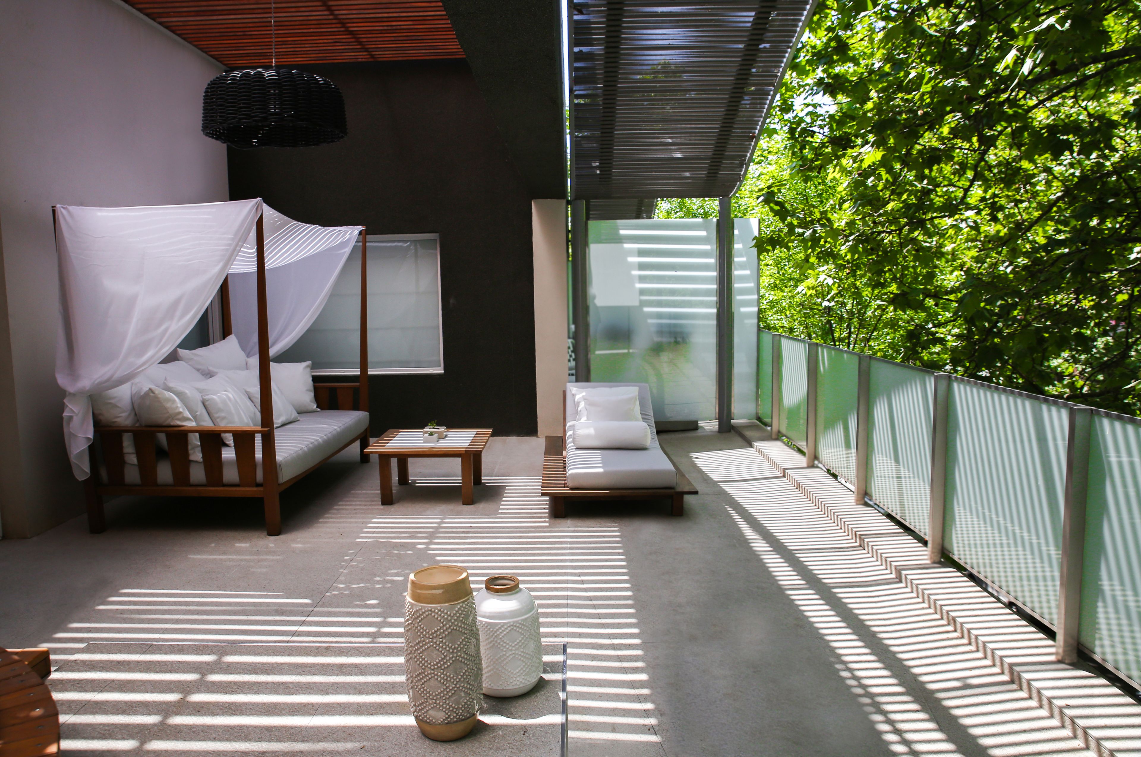 A modern outdoor lounge area with a wooden sofa, a daybed, and a small table.