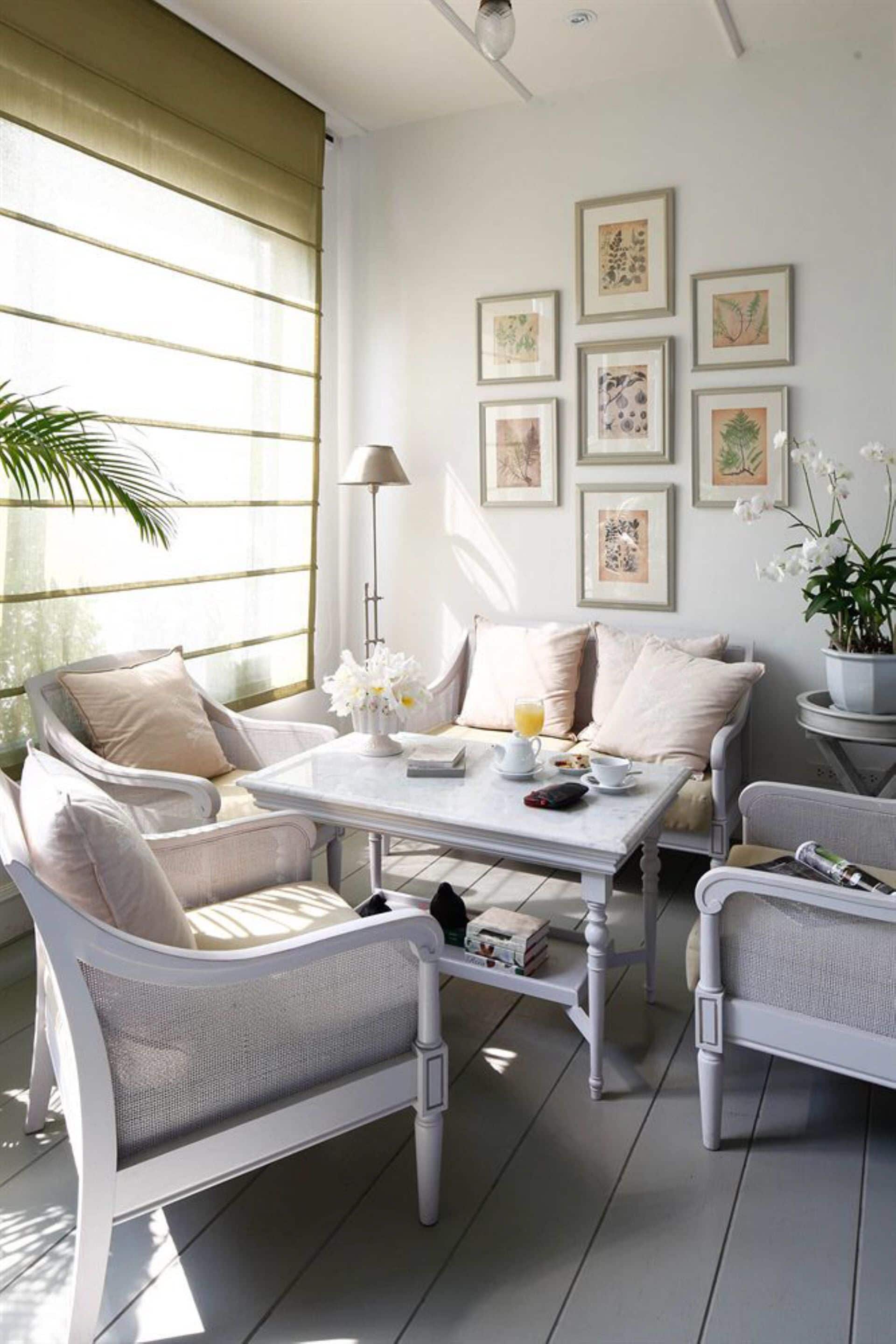 Una habitación luminosa con una mesa blanca, sillas acolchadas y arte botánico enmarcados en la pared.