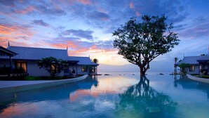 Un resort con piscina que refleja un atardecer, rodeado de edificios con tejados de azulejos.