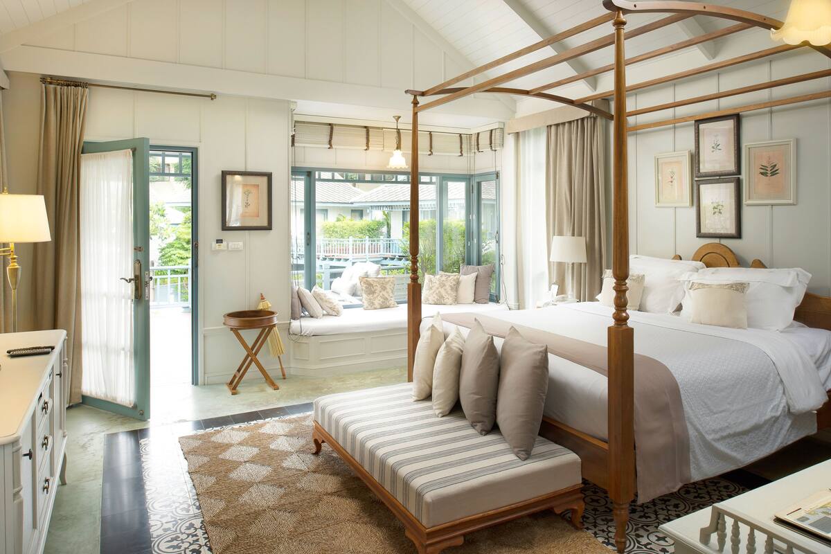 Una cama con dosel de madera, un banco al pie de la cama y vistas a un balcón con mobiliario exterior.