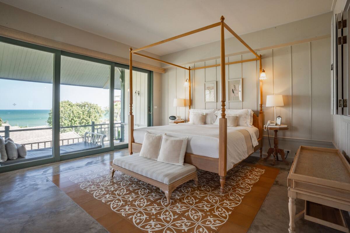 Un dormitorio amplio con cama con dosel, un banco y vista al océano.