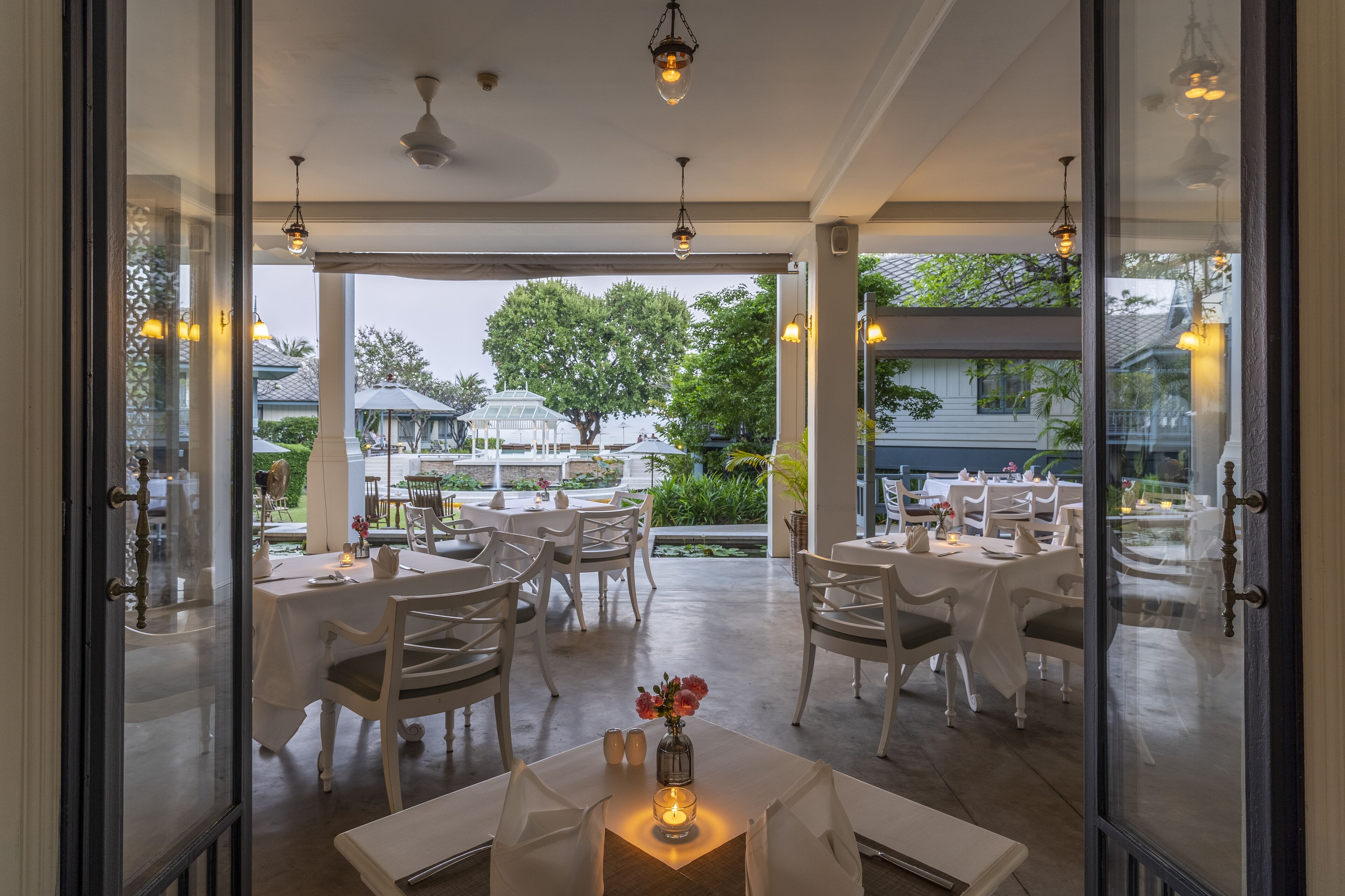 An indoor dining area with tables set for guests, a candle centerpiece, and a view of the outdoor patio.