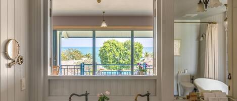 Un baño con un ventanal grande, dos lavamanos con grifos antiguos, un espejo y vista al mar.