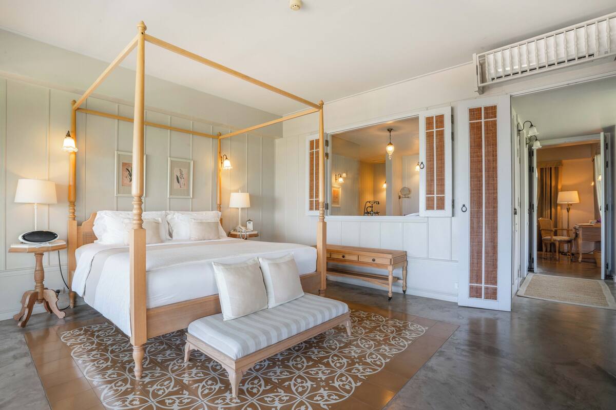 Una cama con dosel de madera, un banco y un tapete estampado en una habitación de hotel.