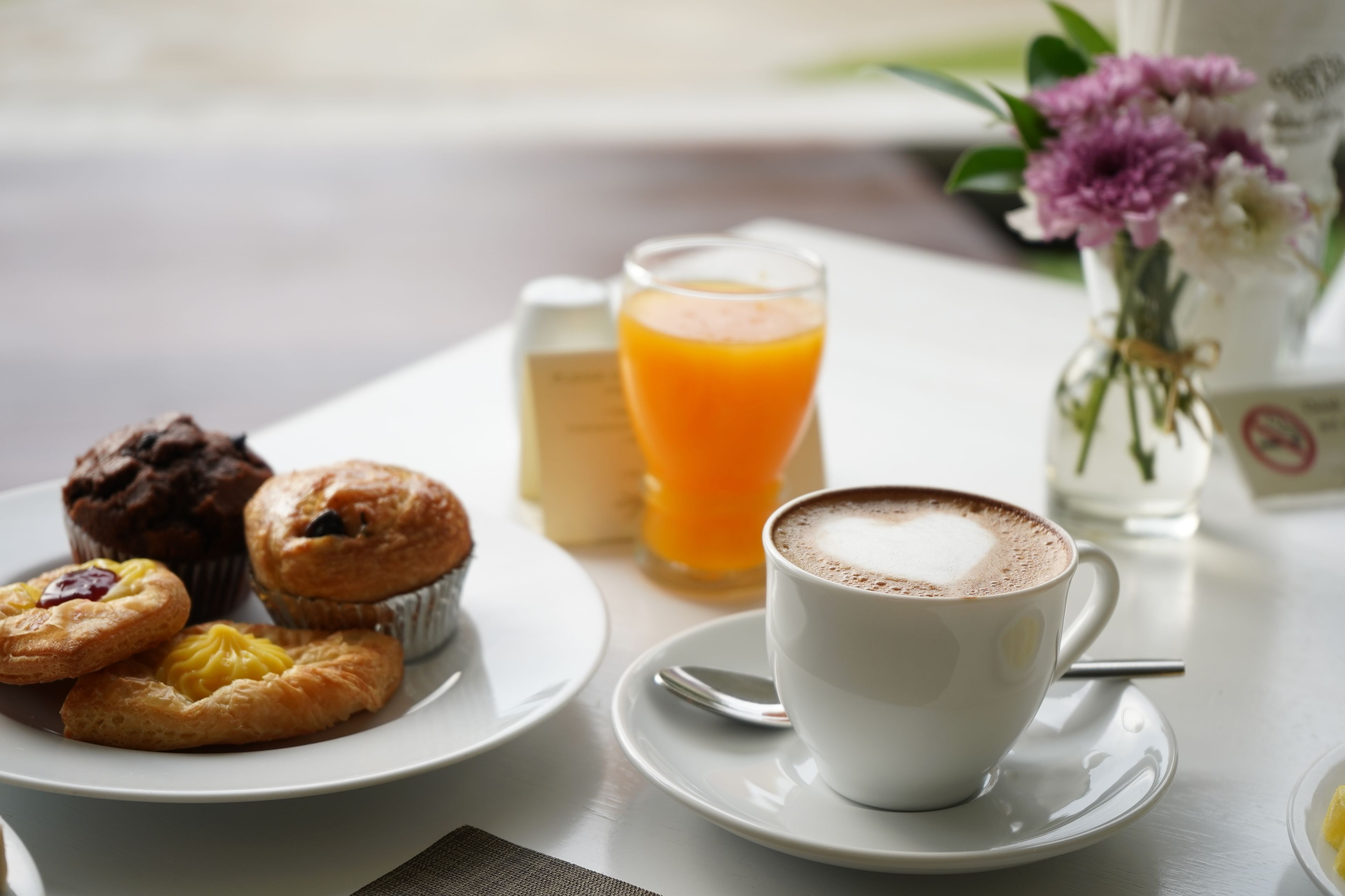 En morgenmadsopsætning med bagværk, et glas appelsinjuice og en kop kaffe på et bord.