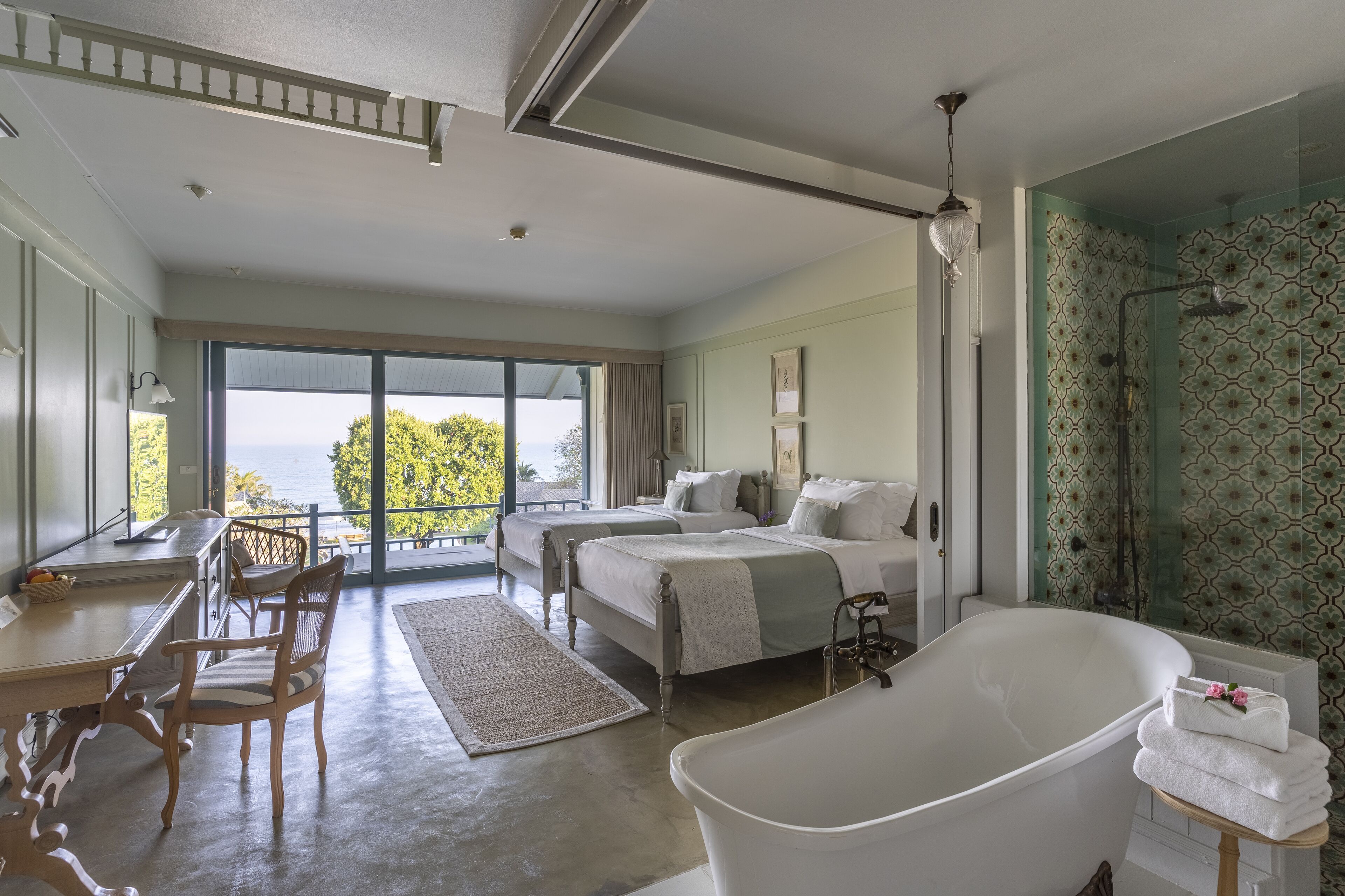 A spacious bedroom with a large bed, a separate sitting area, a bathtub, and a view of the outdoors.