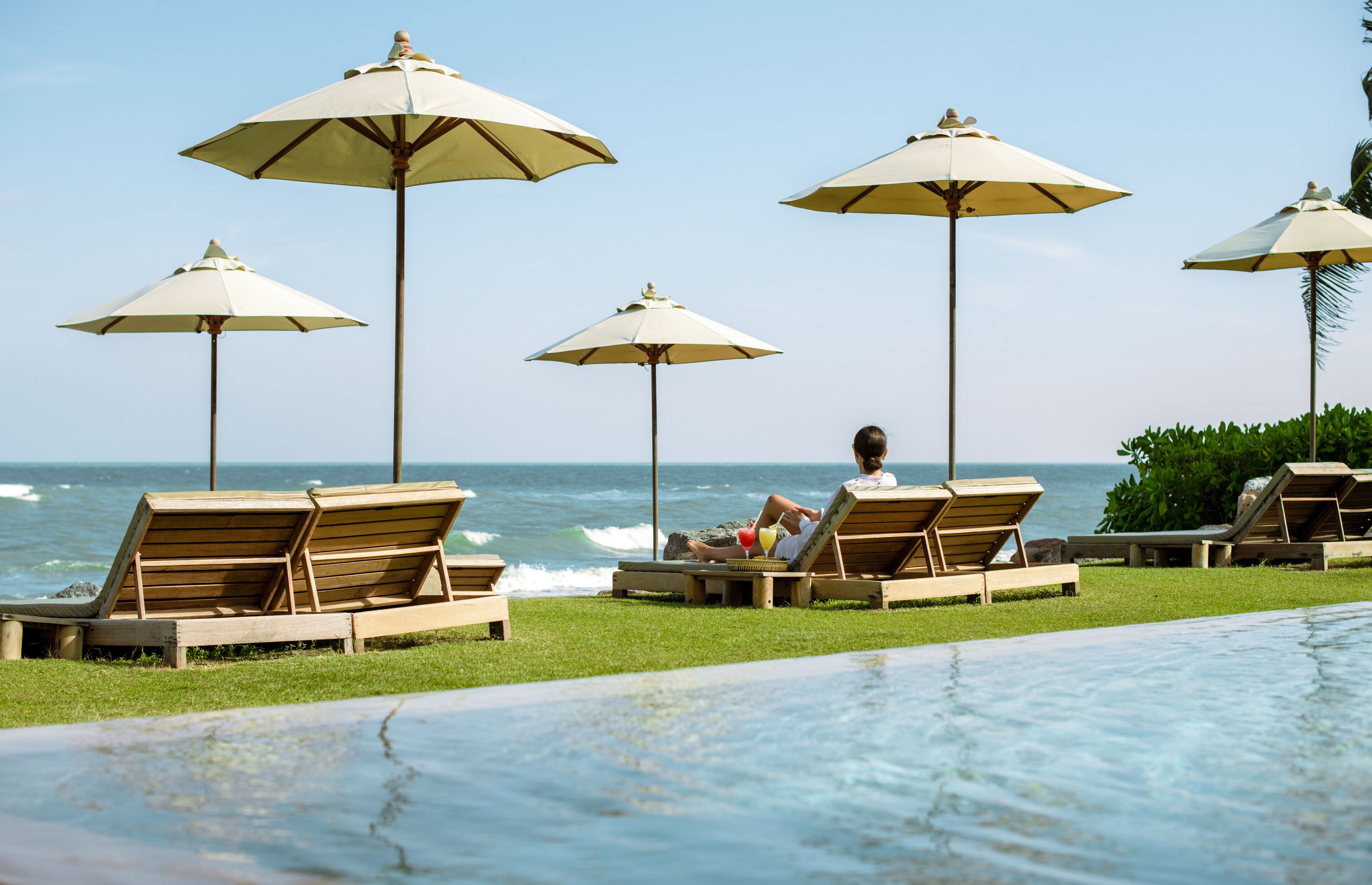 A poolside area with lounge chairs and umbrellas, overlooking the ocean.
