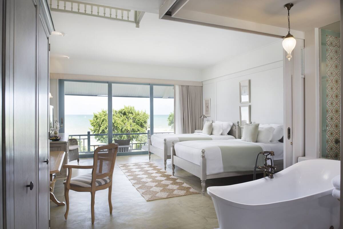 Un dormitorio con dos camas, un ventanal con vistas, una bañera y un comedor también con vistas.