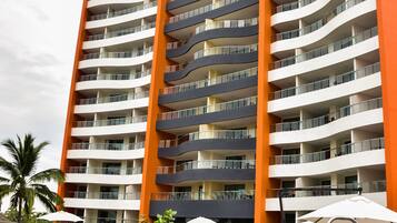A high-rise hotel with multiple balconies, a swimming pool, and outdoor seating areas.