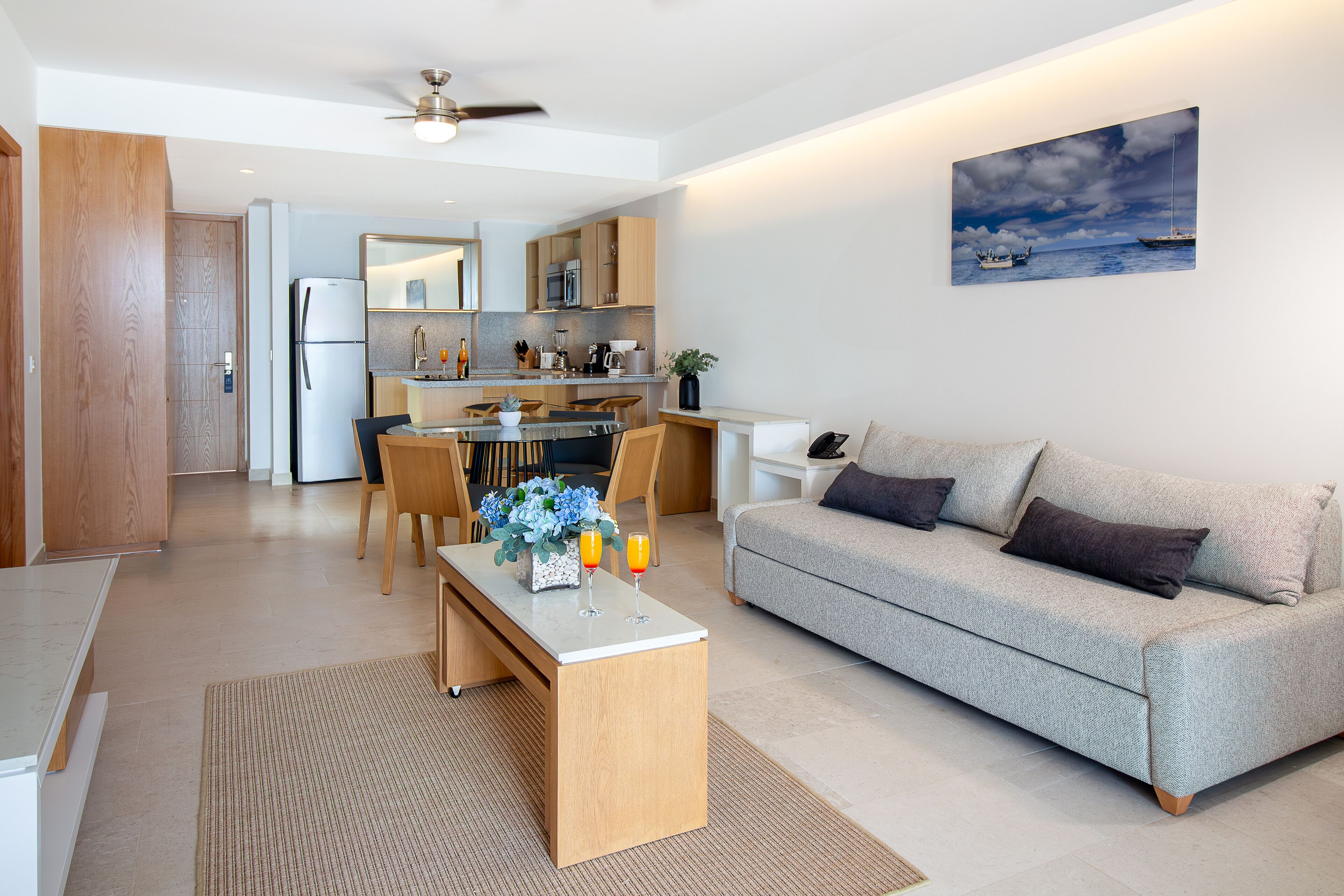 A modern living room with a grey sofa, wooden coffee table, and a dining area with a glass-top table and chairs.
