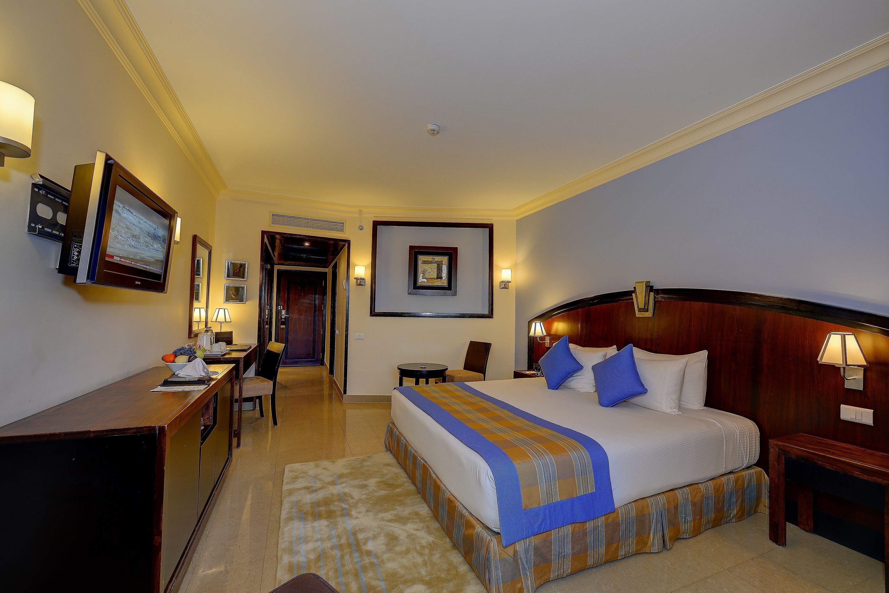 A hotel room with a large bed, a desk, a chair, a small table, and a TV mounted on the wall.