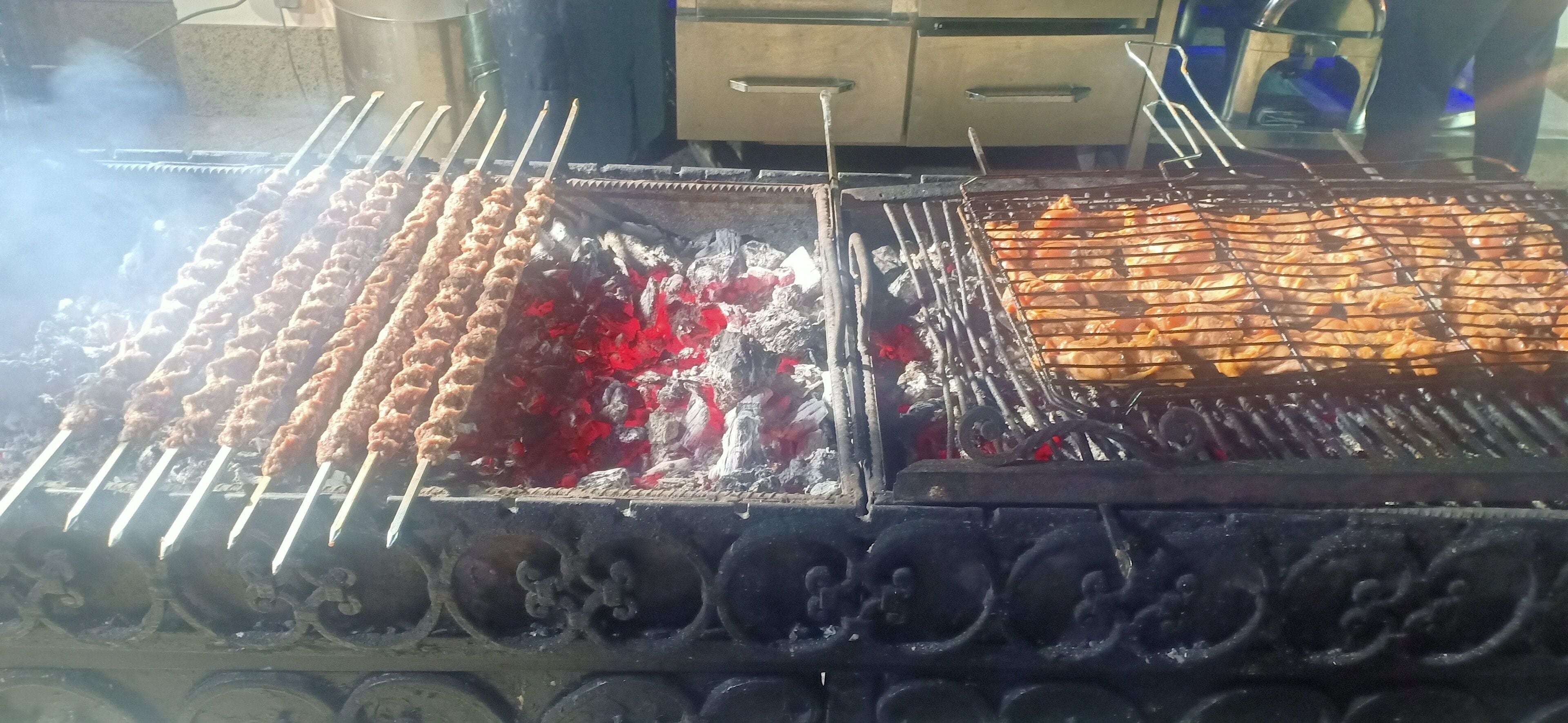 Una parrilla con brochetas de carne asándose sobre carbón.