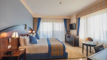 Ein Hotelzimmer mit Bett, Nachttisch, Fernseher, Schreibtisch und einer kleinen Essecke mit Obstschale.