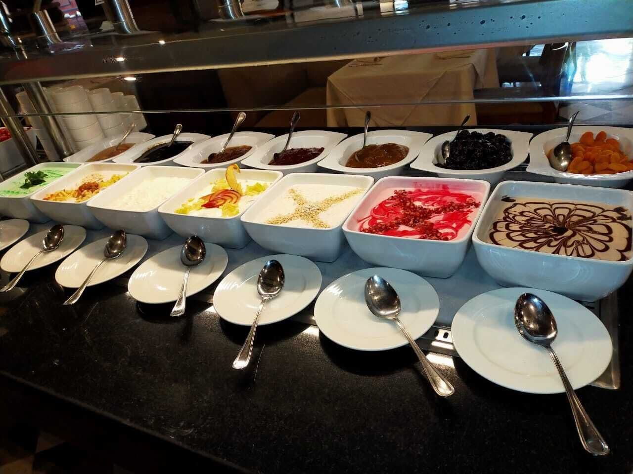 Un buffet proposant divers plats présentés dans des bols et des assiettes, chacun accompagné d'une cuillère.
