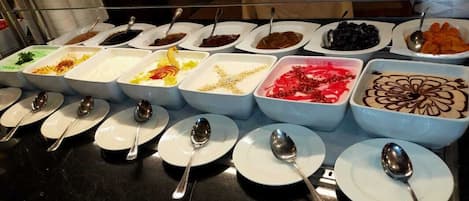 Un buffet proposant divers plats présentés dans des bols et des assiettes, chacun accompagné d'une cuillère.