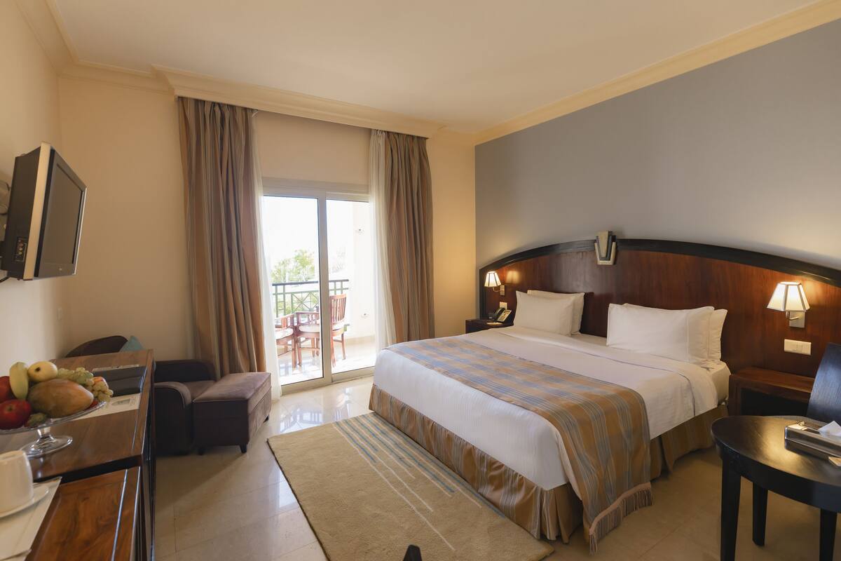 Habitación de hotel con cama, escritorio con fruta, silla, mesa y vista al exterior.