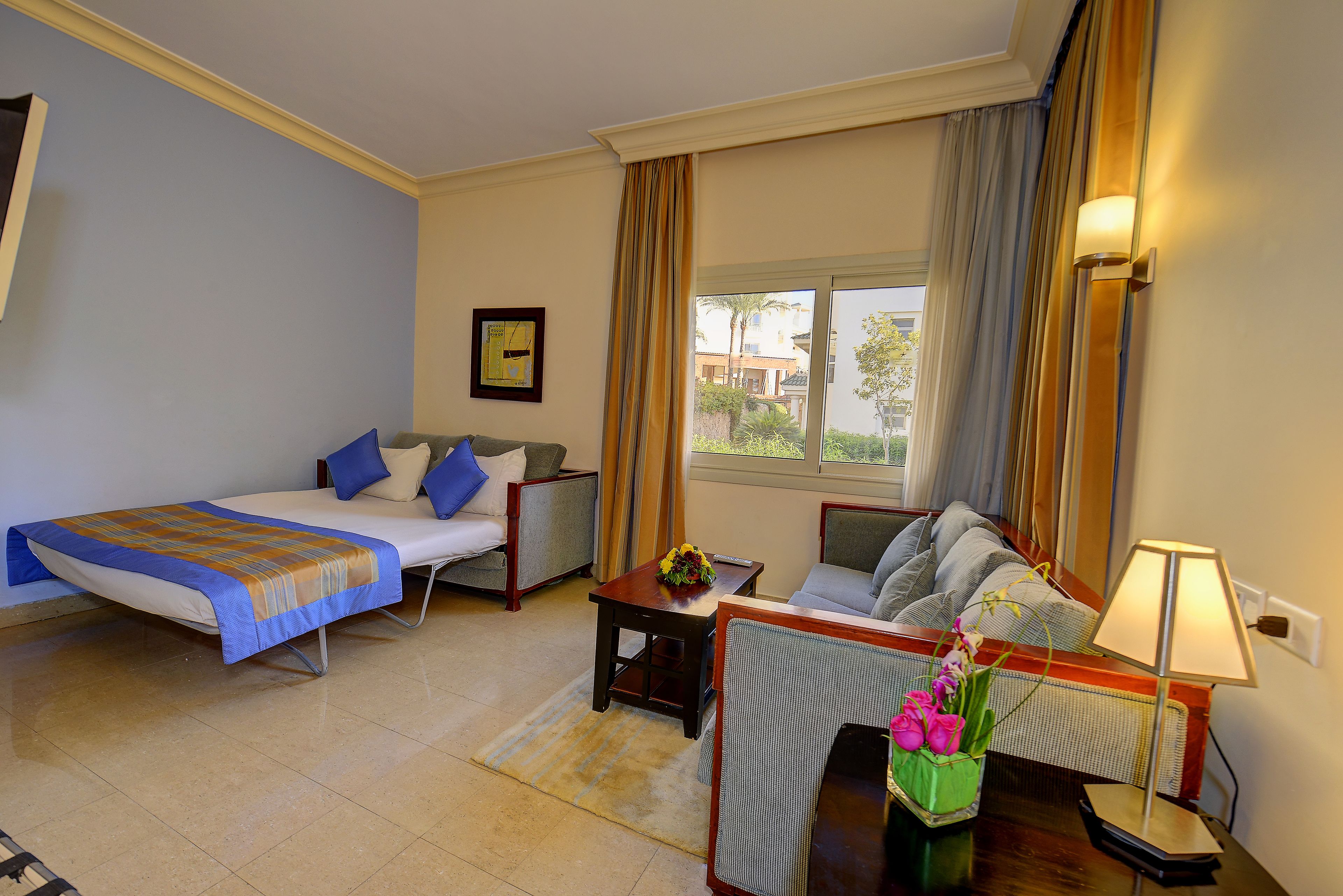 A hotel room with a bed, a sofa, a small table with a vase of flowers, and a lamp.