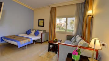 A hotel room with a bed, a sofa, a small table with a vase of flowers, and a lamp.